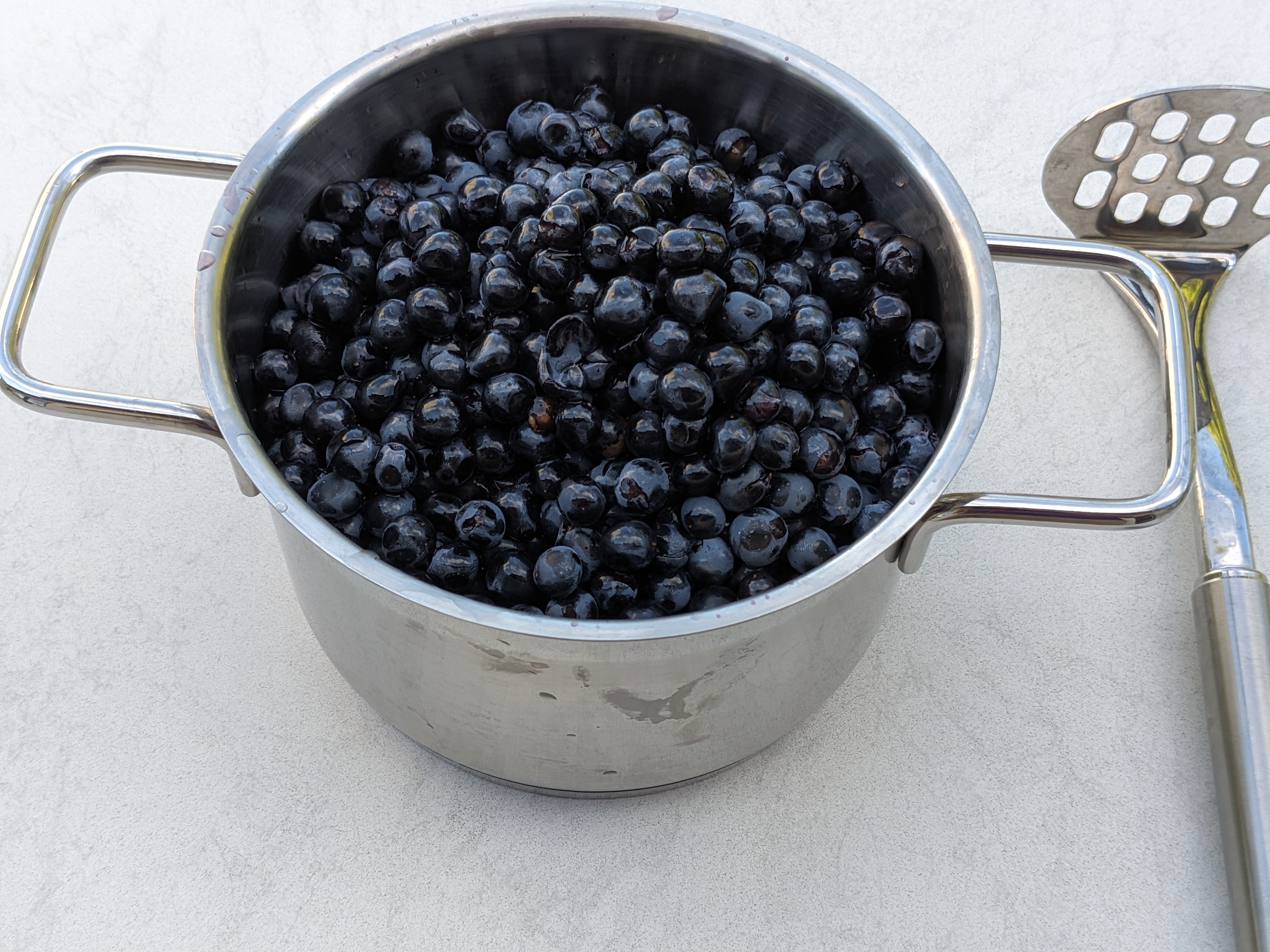 A pot filled to just under the brim with loose grapes. Beside it, a potato masher - always show them the implements, maybe they&rsquo;ll confess.