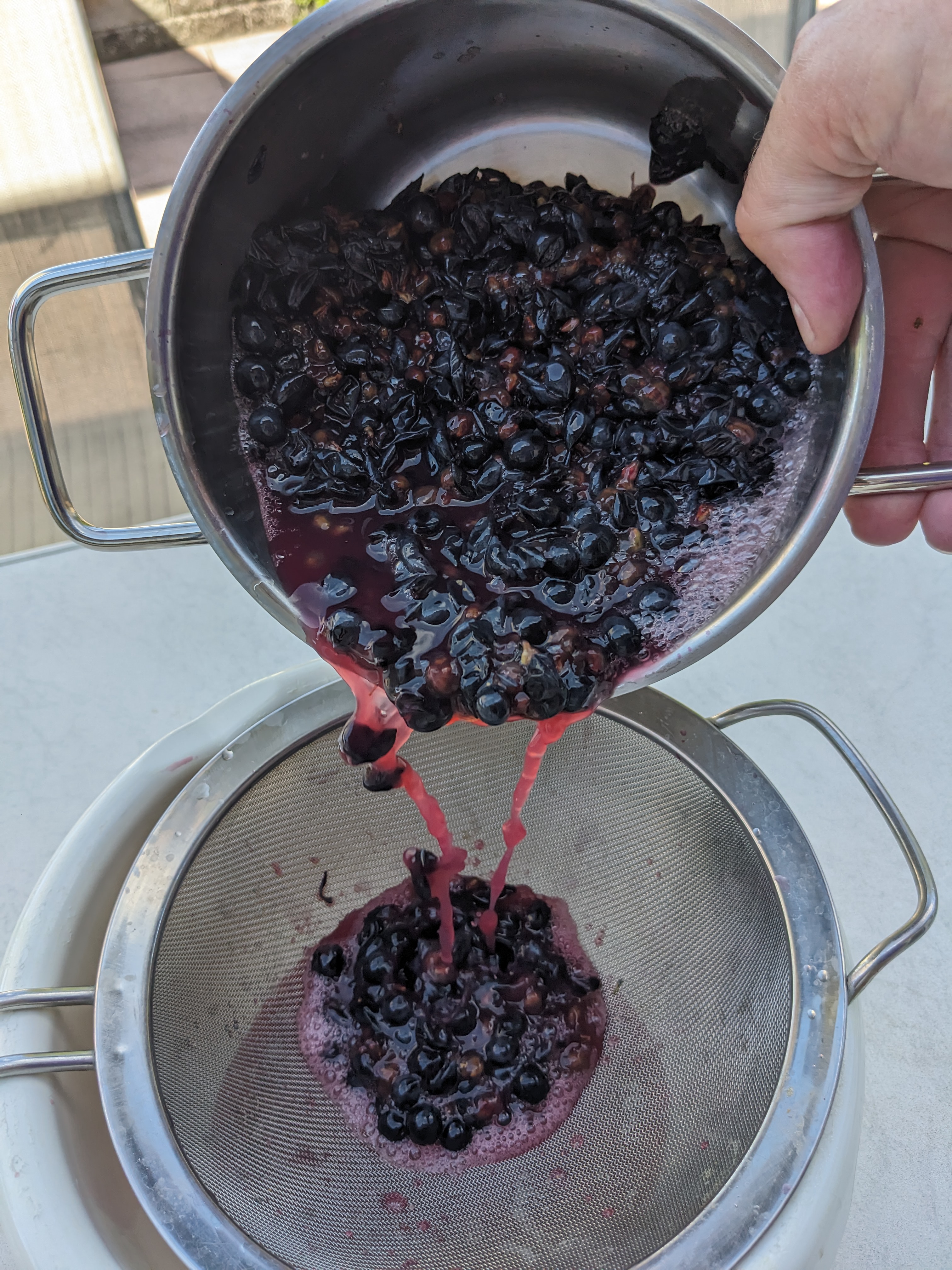 Pouring the pot&rsquo;s contents through a large sieve, removing the skins and seeds.